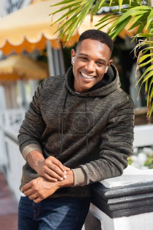 Unbekümmerter Afroamerikaner mit drahtlosen Kopfhörern, der draußen lächelt 