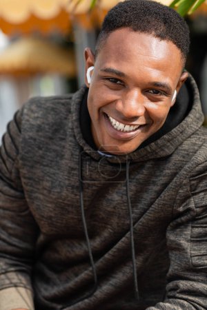 Porträt eines fröhlichen afrikanisch-amerikanischen Mannes mit drahtlosen Kopfhörern, der im Freien lächelt 