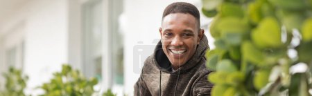 happy african american man in hooded sweatshirt looking at camera outdoors, banner 