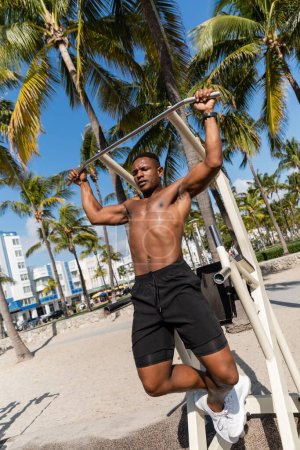 shirtless african american sportsman doing pull ups in outdoor gym in Miami beach 
