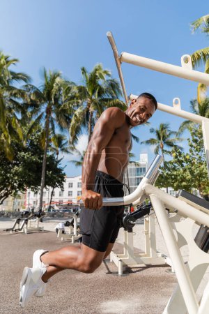 happy african american man in shorts exercising next to palm trees in Miami beach 