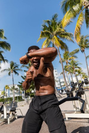 luchador afroamericano emocional y sin camisa en pantalones cortos haciendo ejercicio en Miami Beach 