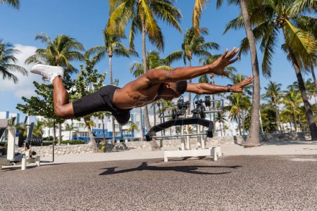 deportista afroamericano sin camisa cayendo al suelo junto a palmeras en la playa de Miami 