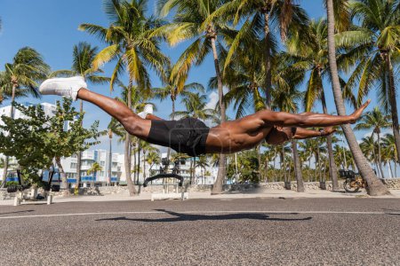 shirtless african american sportsman levitating next to green palm trees in Miami beach 