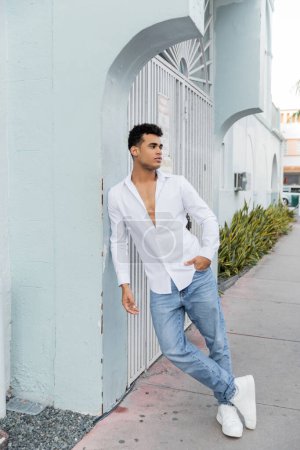 In voller Länge posiert ein hübscher kubanischer Mann in stylischem Hemd und blauer Jeans auf der Straße in Miami