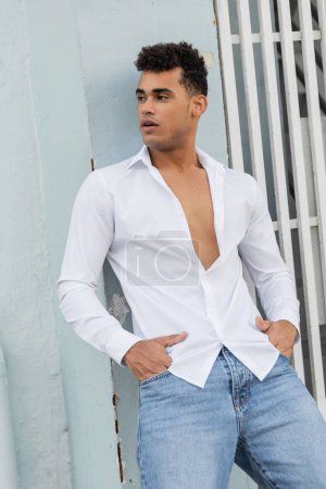 Gut aussehender kubanischer Mann in weißem Hemd und blauer Jeans posiert auf der Straße in Miami, Südstrand