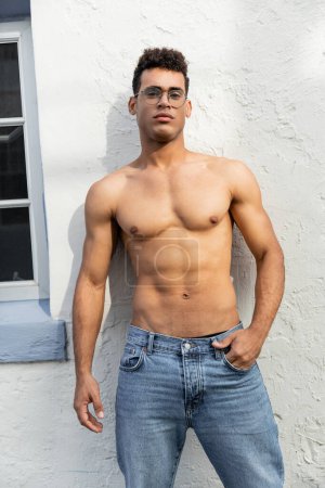 hombre cubano relajado muscular en jeans azules y elegantes gafas redondas posando en Miami