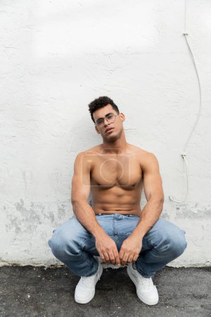 Volle Länge des hemdlosen kubanischen Mannes mit athletischem Körper in stylischer Brille und Blue Jeans 