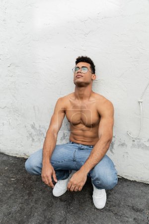 Young and sexy cuban man in stylish eyeglasses and blue jeans on urban street in Miami