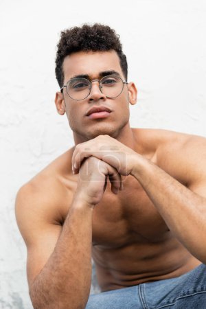 portrait of confident muscular young cuban man in stylish round-shaped eyeglasses looking at camera 