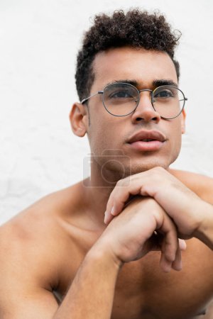 Portrait of shirtless cuban man in round-shaped eyeglasses with curly hair looking away