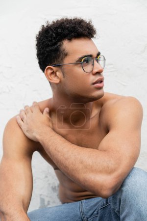 Junger, lockiger kubanischer Mann mit athletischem Körper in Jeans und stylischer, runder Brille