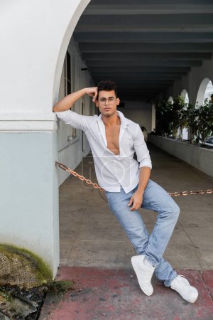 Full length of stylish cuban man in white shirt and jeans on urban street in Miami