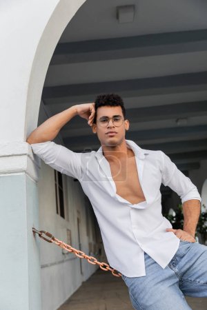 Junger sexy und stylischer kubanischer Mann in weißem Hemd und Brille auf der urbanen Straße in Miami
