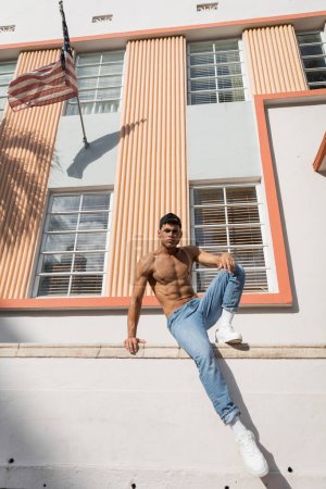 hombre cubano con cuerpo musculoso posando en gorra de béisbol y jeans en la calle en Miami