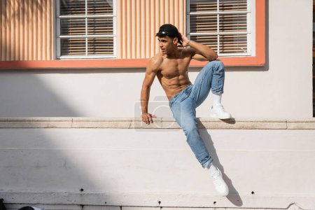 Foto de Joven cubano con cuerpo musculoso posando en gorra de béisbol y jeans en la calle en Miami en verano - Imagen libre de derechos