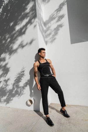 Téléchargez les photos : Sexy jeune homme cubain posant près de mur blanc avec ombre sur la rue urbaine à Miami, plage du sud - en image libre de droit
