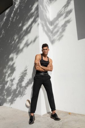 Téléchargez les photos : Pleine longueur de confiant et musclé jeune homme cubain dans des lunettes et tenue à la mode croisant les bras - en image libre de droit