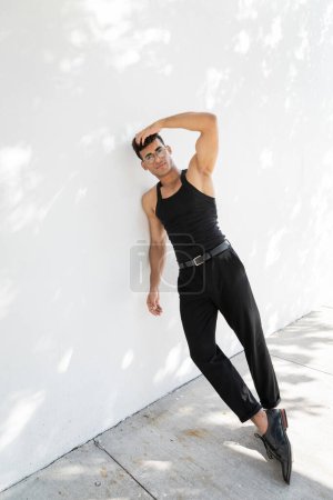 Téléchargez les photos : Jeune homme cubain détendu et musclé en lunettes et tenue noire touchant la tête - en image libre de droit