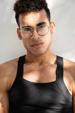 Young and stylish cuban man in eyeglasses and sleeveless t-shirt looking at camera 