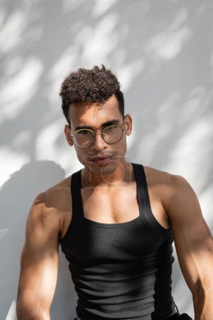 Téléchargez les photos : Portrait d'homme cubain en lunettes et tenue noire tendance près du mur avec ombre et soleil - en image libre de droit