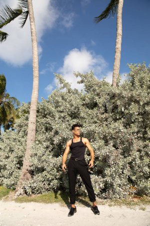 cuban man in black outfit and eyeglasses standing near palm trees on beach in Miami