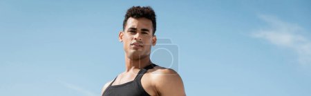 Téléchargez les photos : Jeune homme cubain musclé en tenue noire posant avec ciel sur fond, bannière - en image libre de droit