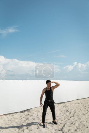 Muscular and young cuban man in stylish outfit covering face from sunlight in Miami, south beach