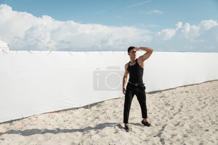 Joven y fuerte hombre cubano en traje negro cubriendo la cara con la mano en Miami, playa sur