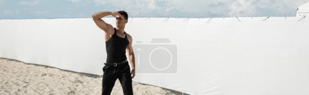 Téléchargez les photos : Homme cubain musclé en tenue noire couvrant le visage avec la main à Miami, plage sud, bannière - en image libre de droit
