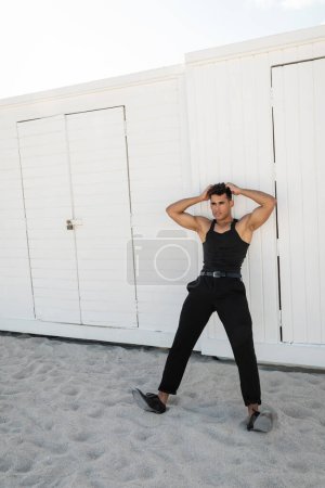 Relaxed and muscular young cuban man in black outfit touching head in Miami, south beach