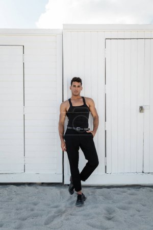 schöner junger kubanischer Mann in schwarzem Outfit posiert in Miami am Südstrand und blickt in die Kamera