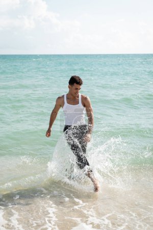 Lächelnder und muskulöser junger kubanischer Mann hat Spaß, während er im Ozeanwasser am Miami South Beach steht