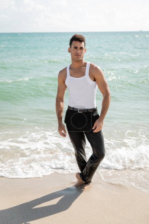 Kubaner blickt in die Kamera, während er auf Sand in der Nähe von Ozeanwasser in Miami steht
