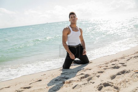 junger kubanischer Mann in stylischer Kleidung posiert am Küstensand in Meeresnähe und in Miami South Beach, Florida