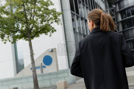 Téléchargez les photos : Vue arrière de la jeune femme élégante et blonde en veste noire marchant à Berlin, Allemagne - en image libre de droit