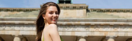 Smiling woman looking at camera while standing near Brandenburg Gate in Berlin, Germany, banner 