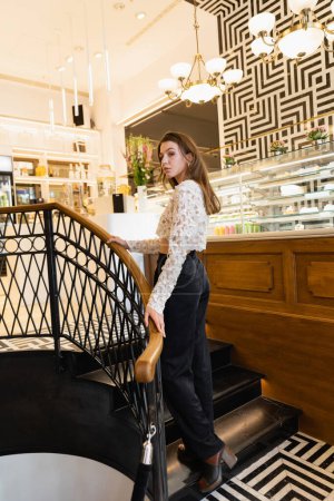 Junge, stylische blonde Frau in Spitzentop und Hose steht in einem modernen Café in Berlin