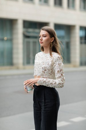 Photo for Fashionable young and fair haired woman in white lace top and pants holding coffee to go - Royalty Free Image