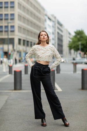 young woman posing in lace top and high waist pants standing on street in Berlin, Germany
