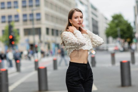 pretty young woman posing in lace top and high waist pants standing on street in Berlin, Germany