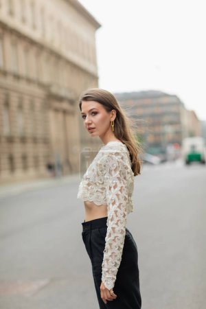 young woman in lace top and high waist pants standing on street in Berlin, Germany 