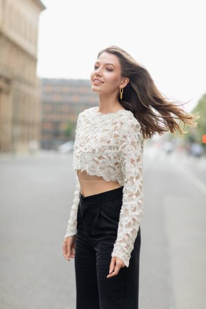 Confident and smiling young woman in white lace top and high waist pants in Berlin, Germany 