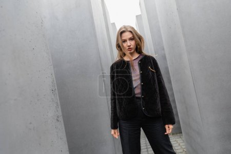 Trendige junge Frau in Jacke steht zwischen dem Denkmal für die ermordeten Juden Europas in Berlin 