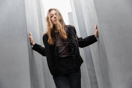 blonde Frau in schwarzer Jacke steht zwischen dem Denkmal für die ermordeten Juden Europas in Berlin