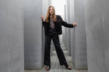 Stilvolle junge Frau in Jacke steht zwischen dem Denkmal für die ermordeten Juden Europas in Berlin