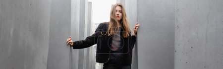 blonde junge Frau in Jacke steht zwischen Denkmal für ermordete Juden Europas, Transparent