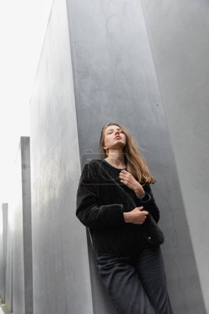 young fair haired woman in jacket standing between Memorial to Murdered Jews of Europe in Berlin