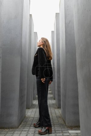 Photo for Woman in black jacket looking away while standing between Memorial to Murdered Jews of Europe - Royalty Free Image