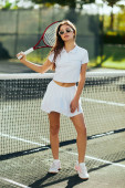 tennis court, active lifestyle, pretty young woman standing confidently in white outfit and sunglasses while holding racket near tennis net, blurred background, iconic city, Miami, sunny day  magic mug #658652248